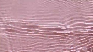 Su yüzeyi üst görünümü. Su pembe renkte sıçrıyor. Saf mavi su, güneş ışığını yavaş çekimde yansıtıyor. Güneş ve gölgeler. Hareket temiz yüzme havuzu dalgalanmaları ve el sallama. 4k