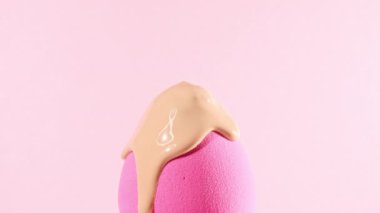 Süngerin üzerine dökülen makyaj sıvısı bej fondöten, yakın plan. Makyaj fırçasının üzerine pembe arka planda kozmetik damlatma kremi. Macro Shot. Güzel makyaj konsepti.