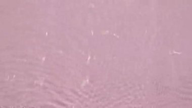 Su yüzeyi üst görünümü. Su pembe renkte sıçrıyor. Saf mavi su, güneş ışığını yavaş çekimde yansıtıyor. Güneş ve gölgeler. Hareket temiz yüzme havuzu dalgalanmaları ve el sallama. 4k