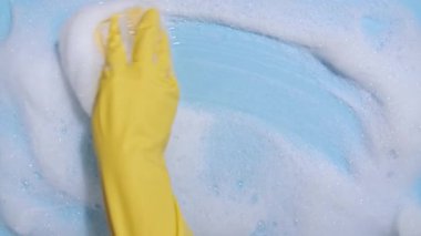 Sarı lastik bir eldiven, temiz bir sünger tutar ve mavi arka planda sabunlu bir köpüğü siler. Temizlik konsepti, temizlik hizmeti. Pankart. Düz yatış, üst görünüm