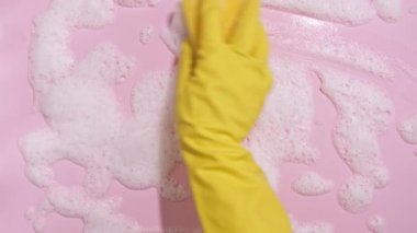 Sarı lastik bir eldiven, temiz bir sünger tutar ve pembe arka planda sabunlu bir köpüğü siler. Temizlik konsepti, temizlik hizmeti. Pankart. Düz yatış, üst görünüm