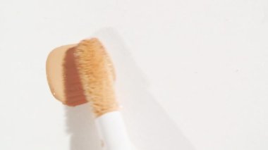 Makro çekim ve ağır çekim fırça, aplikatör, leke, kapatıcı beyaz arka planda izole edilmiş. Profesyonel kozmetik reklamı. Kozmetik sıvı fondöten ya da krem bej rengine yakın çekim.