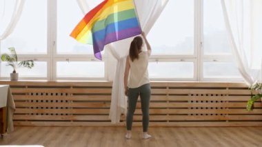 LGBT gay bayrağını elinde tutan ve gün batımında güneşli ışıklarda sallanan bir kadın. Gökkuşağı LGBT bayrağı - Lezbiyen, gey, biseksüel, transseksüel sosyal hareketler.