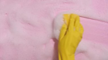 Sarı lastik bir eldiven, temiz bir sünger tutar ve pembe arka planda sabunlu bir köpüğü siler. Temizlik konsepti, temizlik hizmeti. Pankart. Düz yatış, üst görünüm