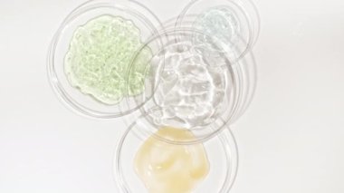 Beyaz arka planda kozmetik numuneleriyle Petri kaplarının rotasyonu. Şeffaf jel sıvısı, köpüklü krema. Kimyasal laboratuvar araştırması. Doğal Organik Kozmetik, İlaç.