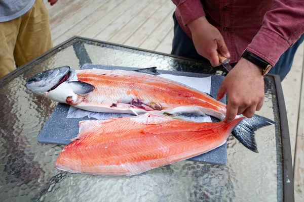 A King Salmon (Chinook) is being fillet on a table. Caught in British-Columbia, this Salmon lives between California and Alaska, and is a very important food source.