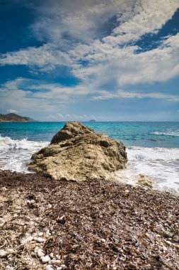 Üzerinde kayalar ve dalgalar olan güzel bir deniz manzarası, mavi gökyüzü ve beyaz bulutlar. Dikey görünüm
