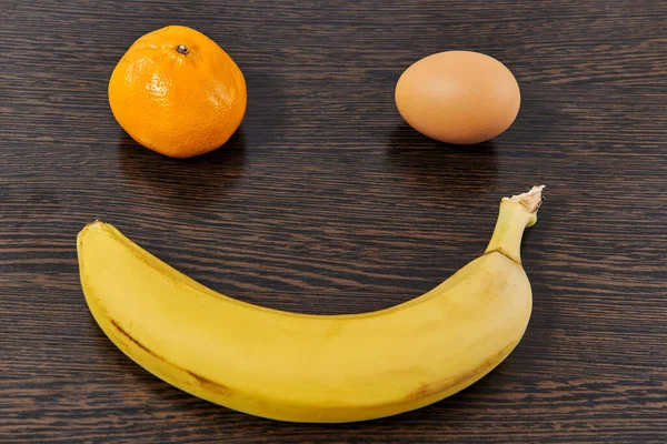 Hafif çizgili arka planda mandalina muz ve tavuk yumurtasından yapılmış gülen surat..