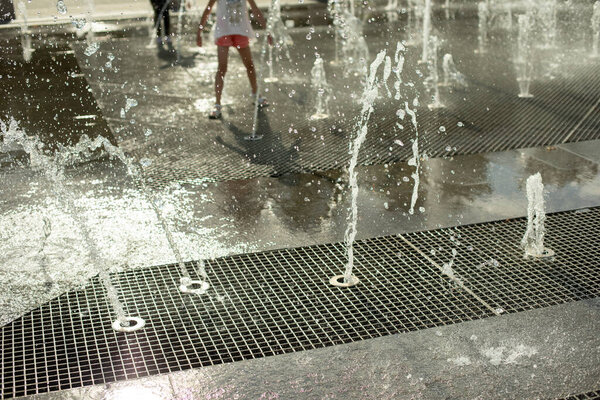 Jets of water on the street. Splashes of a fountain in the town square. Rest in summer on a hot day. Fresh water pours under pressure.