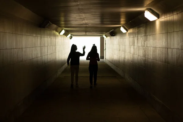 Silhouette of people in the tunnel. The girls walk through an underground tunnel. A long corridor under the road.