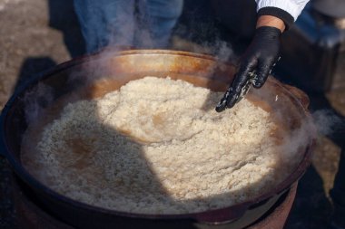 Pirinç pişiriyorum. Aşçı sokakta pilav pişirir. Doğal ışık altında bir şat yiyecek. Pirinçli bir kazan yanıyor. Doğu ülkelerinin ulusal yemeği. Siyah eldivenli aşçı..
