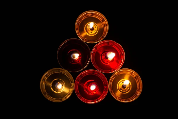 The candles are laid out in a triangle. Candles burn in the dark. Red and yellow wax. The combustion process.
