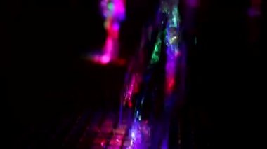 Colored stream of water on dark background. Fountain at night. Jet of water rises up in turbulent stream. Illumination of fountain at night. Video shooting of monotonous movement of liquid.