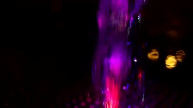 Colored stream of water on dark background. Fountain at night. Jet of water rises up in turbulent stream. Illumination of fountain at night. Video shooting of monotonous movement of liquid.