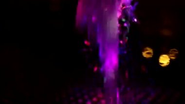 Background colored splashes of water in dark. Flow of water is illuminated by ice LEDs. Drops of liquid of different colors. Texture of fountain flow. Details of urban infrastructure.