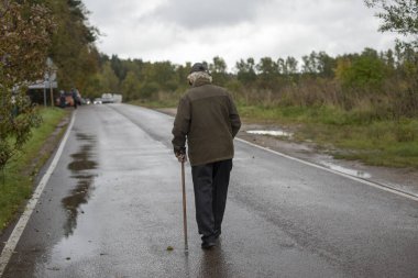 Yaşlı adam yolda yürüyor. Destek için sopası olan emekli. Bacağından yaralanan bir adam. Rusya 'daki dedem parkta yürüyor..