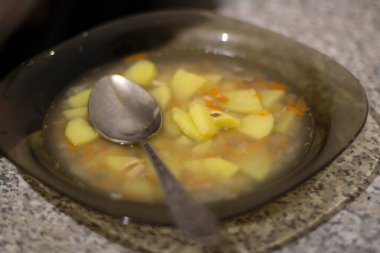 Bir kase çorba. Bir kaşık çorba. Yarısı yenmiş öğle yemeği. Mutfakta yemek var. Tabaklar masaya..