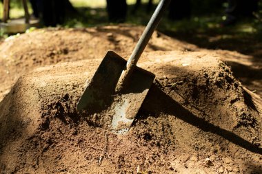 Cenaze levazımatçısı mezara girdi. Kürek ve toprak. Adam toprağı kazıyor. Kum çarpması. Bahçe araçları.