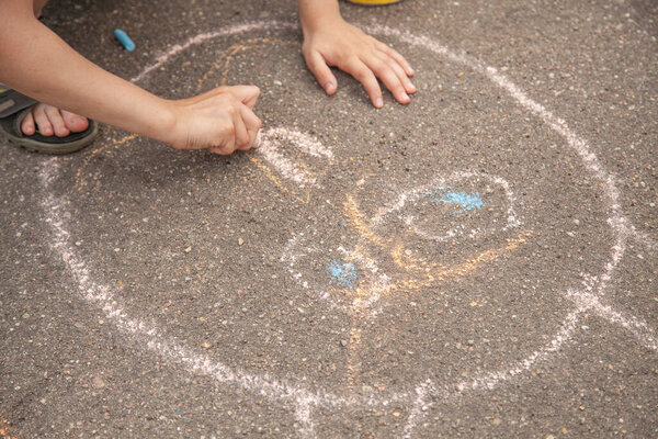 Children draw with chalk on the pavement. The child creates a picture. Children's fine art. Holidays with children in the summer in the city. A quick lesson for the kids. Drawing with colorful crayons.