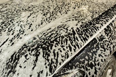 Arabada sabun köpüğü. Siyah arabada beyaz köpük dokusu. Ulaşım yıkama. Yüzeyde yıkama maddesi.