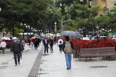Curitiba şehrinde soğuk ve yağmurlu bir öğleden sonra. 1 Nisan 2022, Curitiba, Parana, Brezilya: Yayalar Cuma (1) günü Curitiba, Parana 'da çiseleme ve düşük sıcaklık altında yürürler.). 