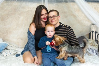 Küçük kızıl saçlı bir çocuk, yatağında annesinin, babasının ve köpeğinin yanında oturuyor. Köpekli mutlu bir aile. Noel zamanı.