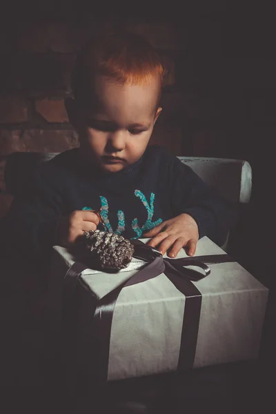 Mutlu, küçük, kızıl saçlı bir çocuk elinde Noel hediyesi olan bir kutuyla kameraya bakmıyor.