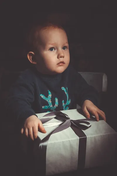Mutlu, küçük, kızıl saçlı bir çocuk elinde Noel hediyesi olan bir kutu tutuyor.