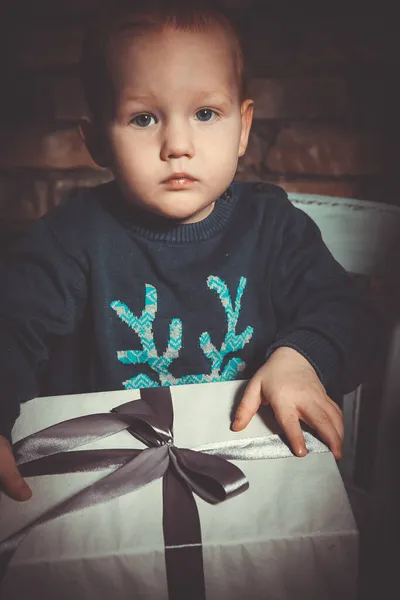 Mutlu, küçük, kızıl saçlı bir çocuk elinde Noel hediyesi olan bir kutu tutuyor.
