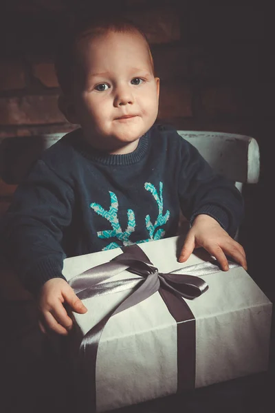 Mutlu, küçük, kızıl saçlı bir çocuk elinde Noel hediyesi olan bir kutu tutuyor.