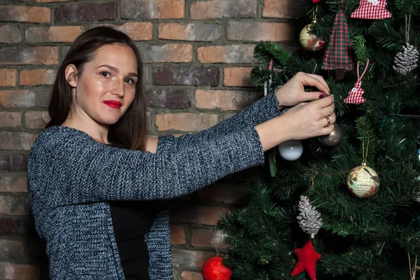 Kırmızı dudaklı güzel kız Noel ağacına bir top asıyor.