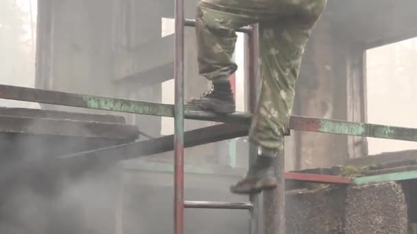 Egy katonai egyenruhás férfi leereszkedik egy vaslépcsőn egy gépfegyverrel a háta mögött. — Stock videók