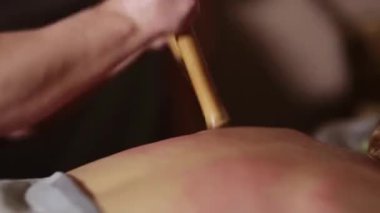 Masaj terapisti, bambu çubuğuyla sırt kaslarına rahatlatıcı bir masaj yapıyor.