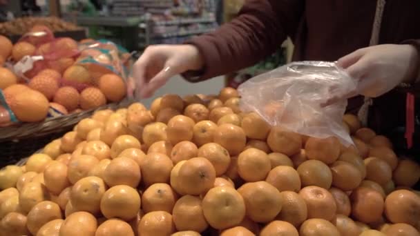 Una chica con una toma y pone mandarinas fragantes frescas en una bolsa de plástico. — Vídeos de Stock
