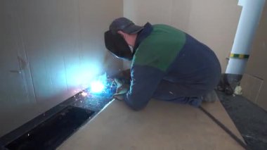 Fabrika işçisi metali kaynaklıyor. Adam kaynak yapıyor. Kaynak makinesi kullanarak argon veya elektrot ile kaynak yapmak. Kıvılcımlar ve parıltılar uçuşuyor.