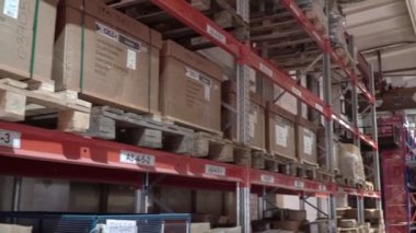 Büyük fabrika deposu. Dükkan koridorları. Kamera büyük bir mağazanın içinde döner. Depoya teslimat var. Kutuları ve malları taşımak için forklift kullanan lojistik işleri ve aracı. kargo posta endüstrisi