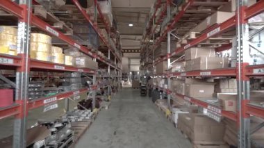 Büyük fabrika deposu. Kamera büyük bir mağazanın içindeki raflar arasında döner..