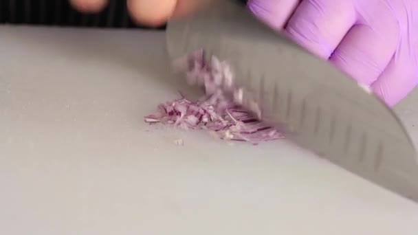 Close-up tiro de cebola roxa finamente picado com faca de aço na placa de corte branco — Vídeo de Stock