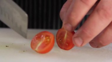 Aşçı büyük bir mutfak bıçağıyla domatesleri keser. Kimliği belirsiz bir adam elinde bıçakla masada taze sebze salatası hazırlarken kiraz domateslerini kesiyor. Yemek hazırlama. Sağlıklı yemek. Doğranmış domates