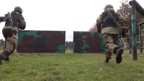 Soldaten in Helmen und kugelsicheren Westen mit Maschinengewehren auf dem Rücken springen über ein Hindernis. Wand. — Stockvideo