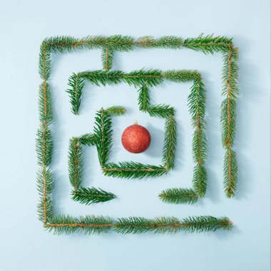 Taze yeşil köknar dallarıyla yapılmış doğal labirent ve parlak mavi arka planda kırmızı Noel mücevheri. Yaratıcı doğa konsepti. Yeni Yıl Kutlama Planı.