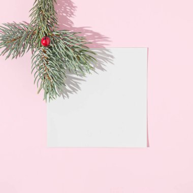 Noel ağacı dalı ve pastel pembe arka planda beyaz kağıt not. Asgari yeni yıl konsepti. Düz yatıyordu.
