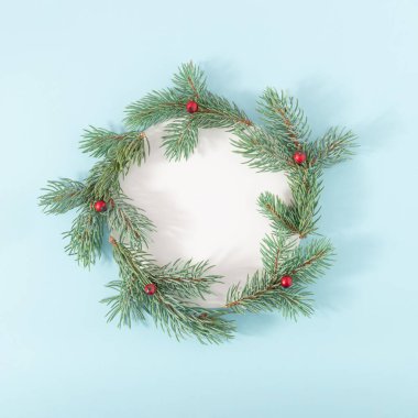 Kırmızı böğürtlenli köknar dallarından ve parlak mavi arkaplanlı beyaz kağıt kartlardan oluşan Noel çerçevesi. Yaratıcı kış tatili kompozisyonu. Düz yatıyordu.