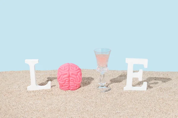 Word LOVE with brain toy and wine glass on beach sand. Minimal love concept. Sunshine shadows.