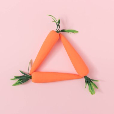 Pastel pembe arka planda havuç üçgeni çerçevesi. Asgari Paskalya konsepti. Bahar sebzeleri.