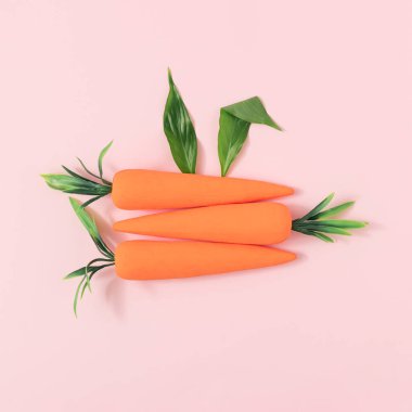 Taze yeşil yapraklardan yapılmış tavşan kulakları ve pastel pembe arka planda havuçlar. Asgari Paskalya konsepti. Bahar tatili planı.