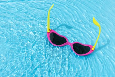 Renkli kalp, parlak mavi suda güneş gözlüğü şeklindeydi. Minimum yaz konsepti. Moda havuzu ya da plaj partisi estetiği. Kopya alanı ile eğlenceli tatil arkaplanı.