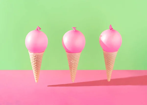 Three ice cream cones with bright pink balloons against vibrant pink and green background. Minimal summer party concept. Creative dessert food idea.