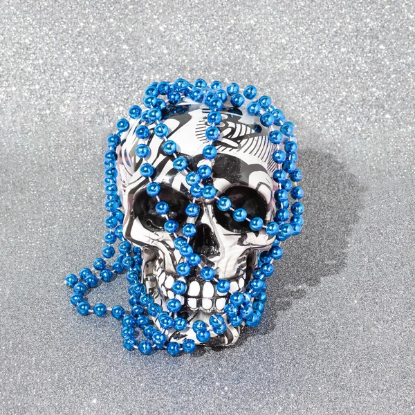 Halloween skull with vivid blue pearls against  glitter shiny grey background. Minimal scary autumn holiday concept.