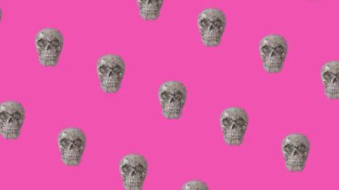 Halloween minimal 4k video loop. Creative pattern made of silver glitter skulls on bold pink background. Trendy holiday concept.